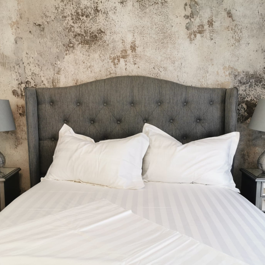Tapet 3D Patina, cu aspect de beton, într-un dormitor cu pat dublu, cu lenjerie de pat albastră, perne decorative și o canapea cu o pătură de blană