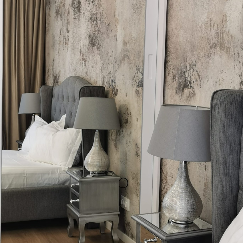 Tapet 3D Patina, cu aspect de beton, într-un dormitor cu pat dublu, cu lenjerie de pat albastră, perne decorative și o canapea cu o pătură de blană