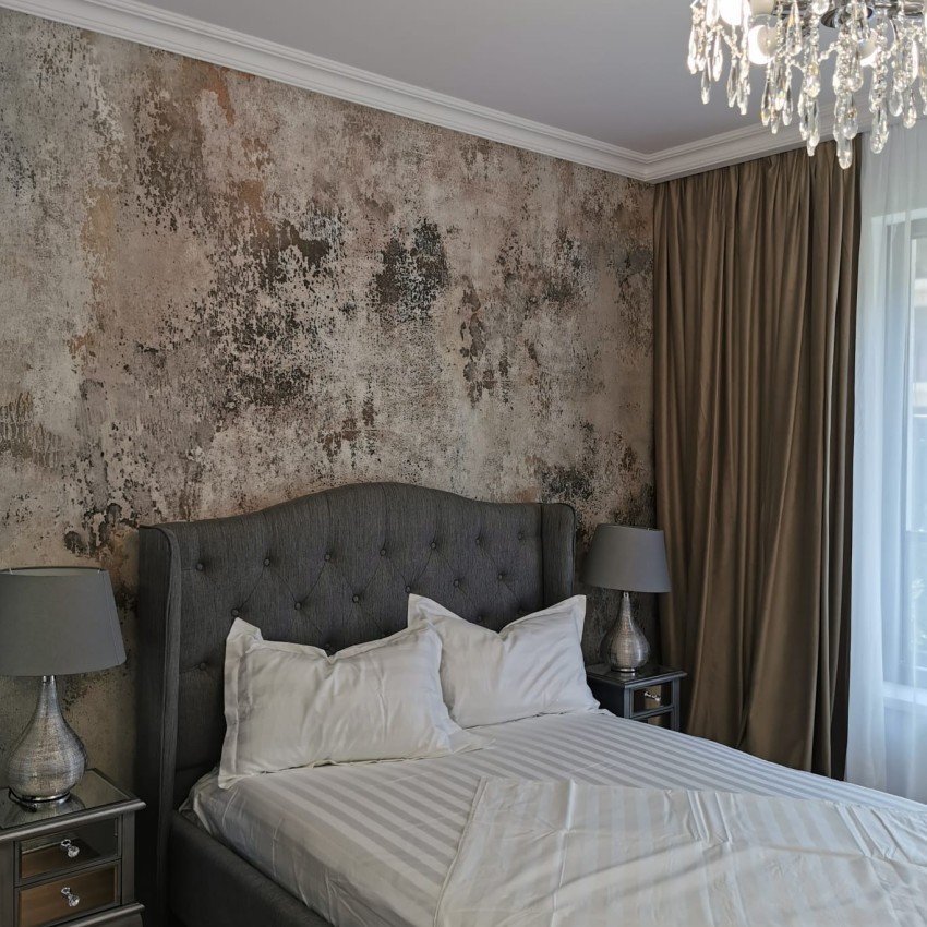 Tapet 3D Patina, cu aspect de beton, într-un dormitor cu pat dublu, cu lenjerie de pat albastră, perne decorative și o canapea cu o pătură de blană