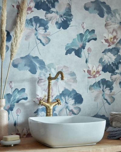 Tapet Water Lilies Blue Dusk Luxury Floral cu flori de nuferi albastre pe fond albastru deschis. Tapetul este decorat cu flori mari si delicate. Se vede un chiuveta alba cu robinet auriu in fata tapetului.