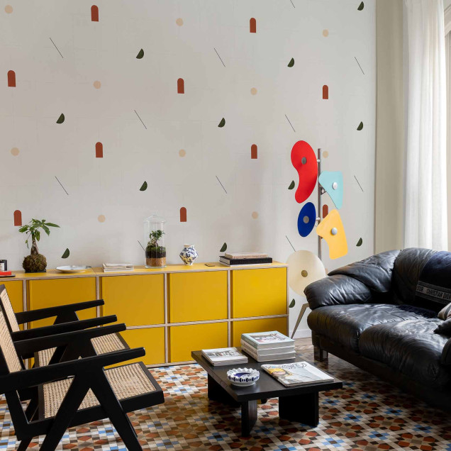 Tapet cu modele geometrice moderne in culori teracota, verde si bej, asezat pe un perete in spatele unui mobilier de living.