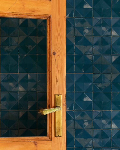 Tapet cu design geometric în nuanțe închise de petrol, alături de o ușă din lemn cu clanță aurie.