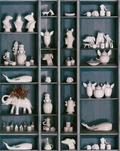 Tapet cu design ceramic faunistic, prezentând diverse obiecte decorative ceramice în formă de animale și figuri, expuse pe rafturi.