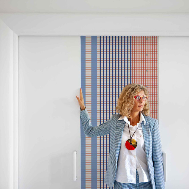 Tapet geometric cu dungi albastre, crem si linii portocalii, asezat pe peretele unei sufragerii moderne.