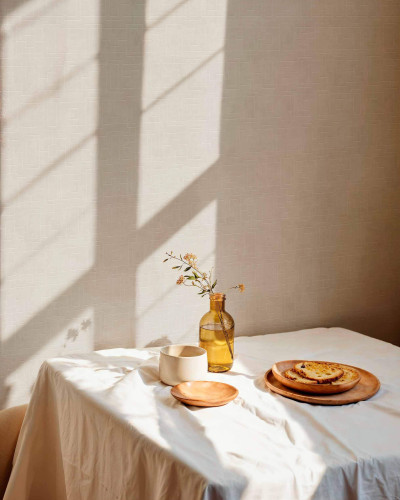 Tapet lavabil cu model geometric Fretwork Limestone, cu o textura fina, gri deschis. Imaginea prezinta o masa cu o fata de masa alba, pe care se afla o vaza cu flori si o cana, pe un fundal de tapet gri.
