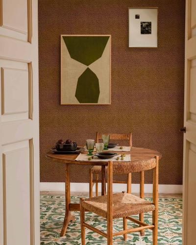 Tapet cu textura de iuta in culoarea cafelei, prezentat intr-un decor de sufragerie cu masa si scaune din lemn.