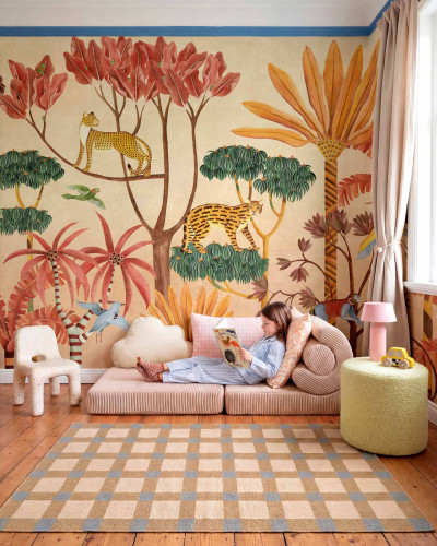 Copil citind pe o canapea în fața unui tapet cu design de junglă, cu feline și plante tropicale.