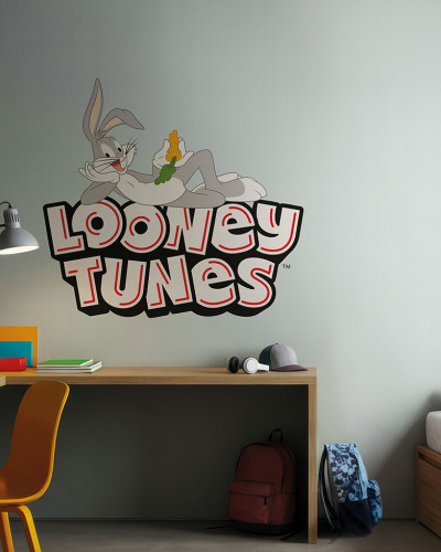 Fototapet Looney Tunes 219 cu Bugs Bunny relaxat pe un perete gri deschis într-o cameră de copii, lângă un birou cu laptop și un pat cu lenjerie colorată.