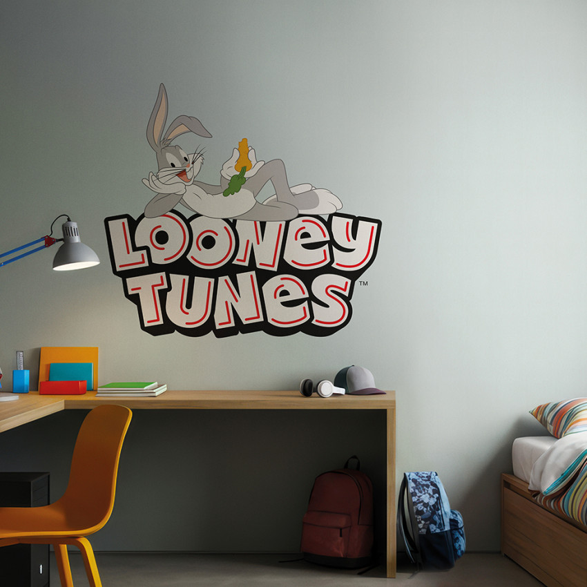 Fototapet Looney Tunes 219 cu Bugs Bunny relaxat pe un perete gri deschis într-o cameră de copii, lângă un birou cu laptop și un pat cu lenjerie colorată.