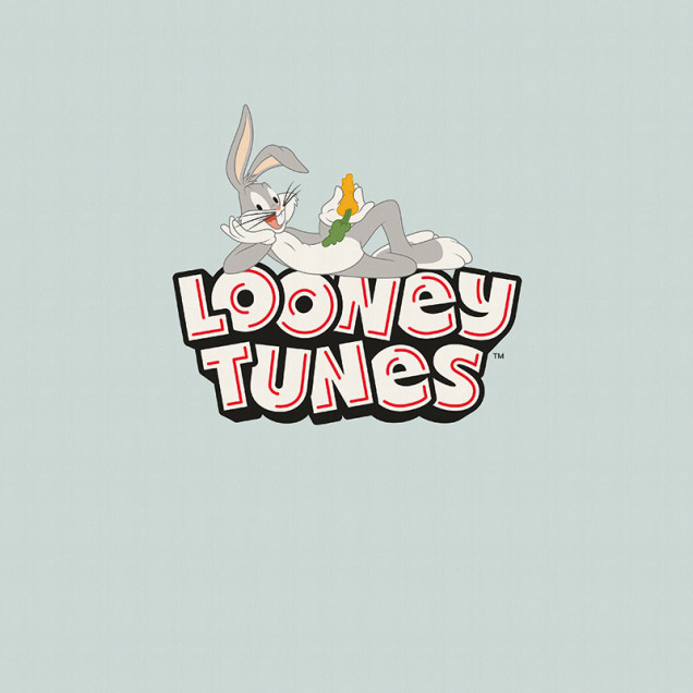 Fototapet Looney Tunes 219 cu Bugs Bunny relaxat pe un perete gri deschis într-o cameră de copii, lângă un birou cu laptop și un pat cu lenjerie colorată.