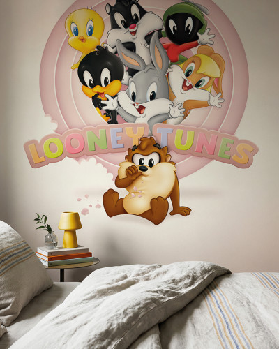 Fototapet Looney Tunes 220 instalat într-un dormitor modern cu pat și noptieră, prezentând Bugs Bunny, Daffy, Tweety, Sylvester, Lola Bunny, Marvin Marțianul și Diavolul Tasmanian pe un fundal roz deschis.