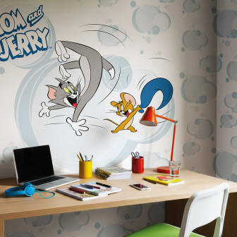 Fototapet Tom and Jerry 108 pe un perete deasupra unui birou de lemn cu un laptop și obiecte de papetărie. Tapetul prezintă pe Tom și Jerry în acțiune, pe un fundal cu nori albastru-gri.