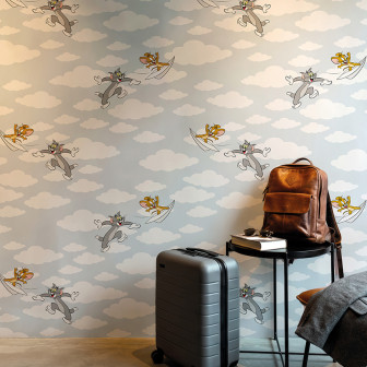 Tapet decorativ Tom și Jerry 102, cu personaje zburând printre nori pe un fundal albastru deschis, într-o cameră modernă cu mobilă maro și gri.