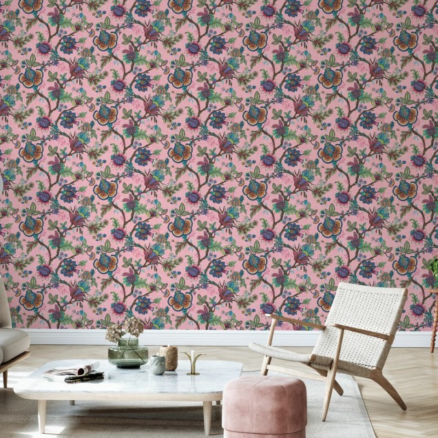 Tapet cu model floral vibrant, in nuante de roz, cu flori colorate si frunze verzi, decorat cu un canapea bleumarin, o masuta de cafea si o planta in ghiveci.