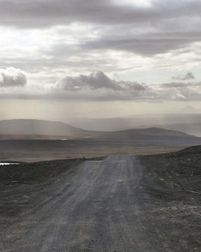 A wallpaper with a scenic view of a winding road in a desolate landscape under a cloudy sky.