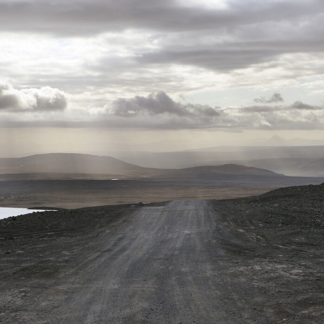 A wallpaper with a scenic view of a winding road in a desolate landscape under a cloudy sky.