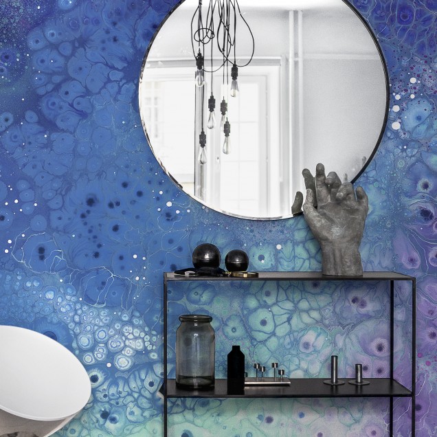 Tapet abstract Aura Aquatic cu modele fluide in nuante de albastru si violet. In imagine este prezentat tapetul montat intr-un dormitor cu un pat modern.