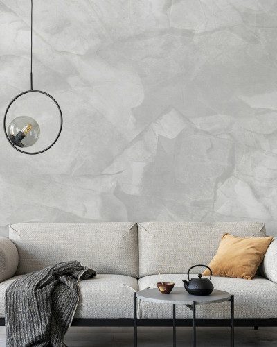 Tapet cu aspect de beton gri deschis, decorat cu un candelabru, o canapea gri si o masuta cu o cana de ceai pe ea.