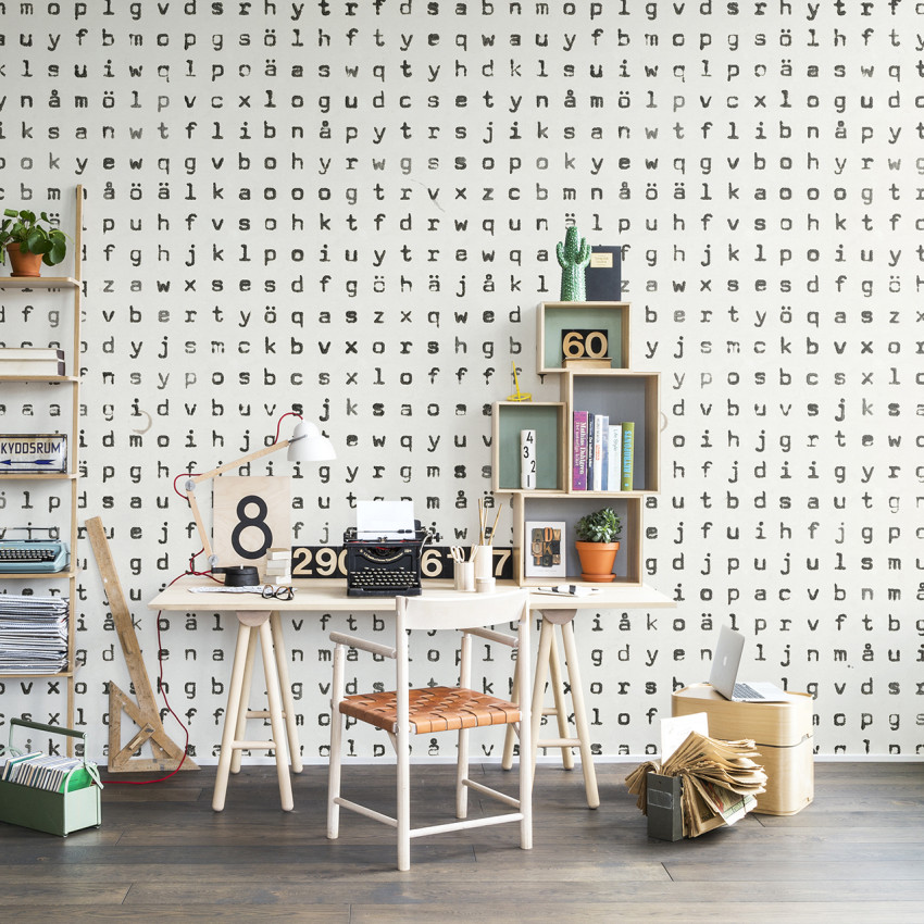Tapet cu design repetitiv, ce prezintă o repetiție de litere. Tapetul este aplicat într-un interior modern, cu un birou, o canapea și plante.