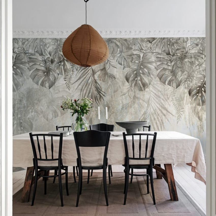 Tapet cu frunze de Monstera într-un interior modern, decorat cu o masă din lemn și scaune negre.