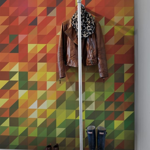Tapet geometric abstract Slanted cu culori calde,  pe un perete din spatele unei canapele negre