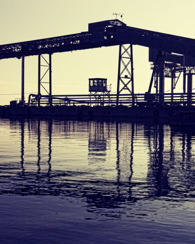 Imagine cu un tapet cu un peisaj al unui port, cu un macaz în siluetă, apus de soare și reflexii ale apei.