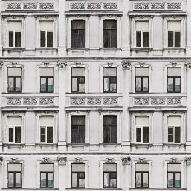 Tapet Rue Relief, Alb, care prezintă o clădire clasică cu ferestre. Tapetul este aplicat pe un perete într-o cameră de luat masa, unde se află o masă rotundă, scaune albe și o plantă.