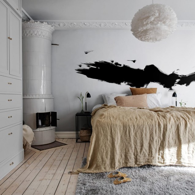 Tapet abstract negru pe fond alb, cu un design minimalist. Tapetul este aplicat pe un perete din sufragerie, deasupra unei canapele gri, cu o masă de cafea din sticlă și un scaun verde.