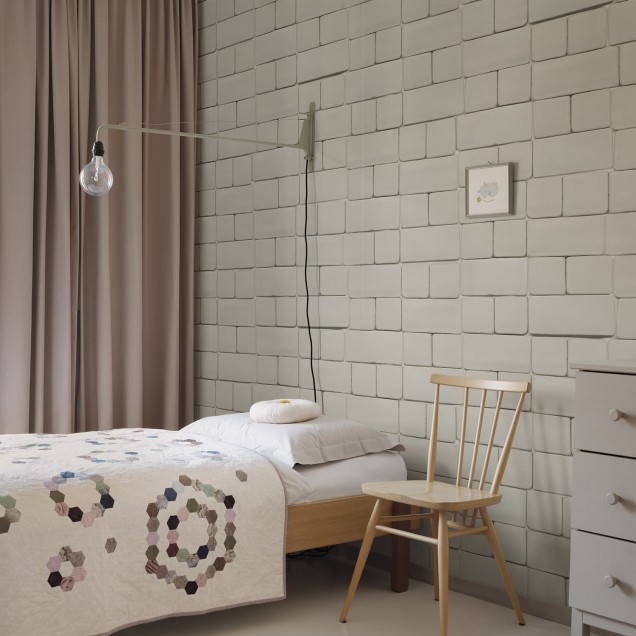 Tapet cu aspect de cărămidă gri, Flight of Tiles, Clay, într-o încăpere cu o masă, un scaun și un dulap cu uși de sticlă.
