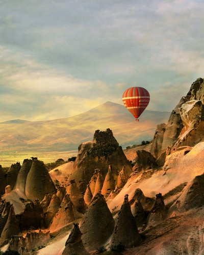 Imagine de fundal cu balon cu aer cald care zboară peste un peisaj stâncos din Cappadocia, Turcia.