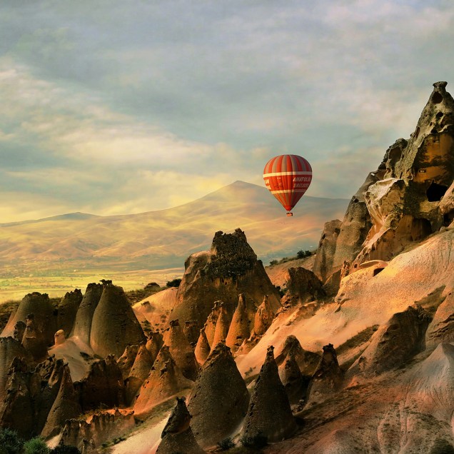 Imagine de fundal cu balon cu aer cald care zboară peste un peisaj stâncos din Cappadocia, Turcia.