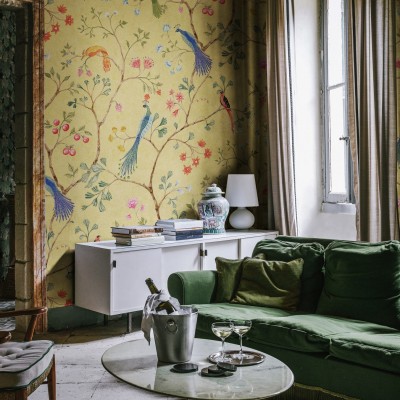 Un interior cu un canapea verde, o masă de cafea și un perete decorat cu un wallpaper cu păsări și flori.