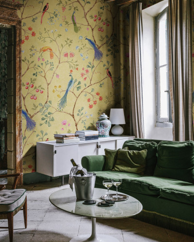 Un interior cu un canapea verde, o masă de cafea și un perete decorat cu un wallpaper cu păsări și flori.