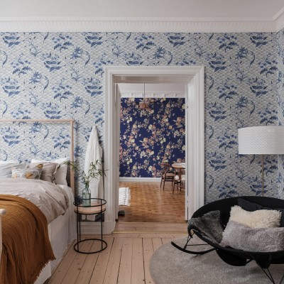 Tapet Floral Ripple, Blue, cu design floral abstract, in nuante delicate de albastru. Imaginea prezinta o camera cu pat si fotoliu, cu tapetul aplicat pe pereti.