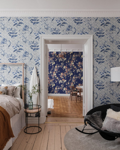 Tapet Floral Ripple, Blue, cu design floral abstract, in nuante delicate de albastru. Imaginea prezinta o camera cu pat si fotoliu, cu tapetul aplicat pe pereti.