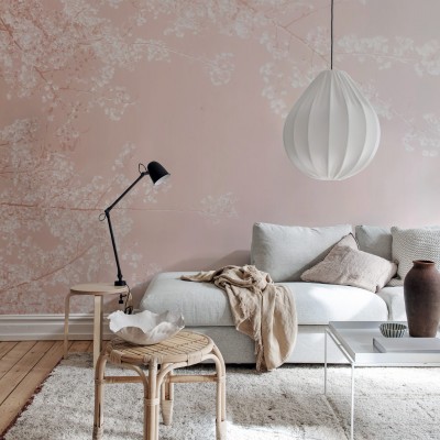 Tapet floral roz cu ramurele delicate pe un fond pastelat. Se vede o canapea alba cu perne si o lampa pe un birou.
