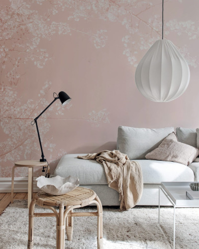 Tapet floral roz cu ramurele delicate pe un fond pastelat. Se vede o canapea alba cu perne si o lampa pe un birou.