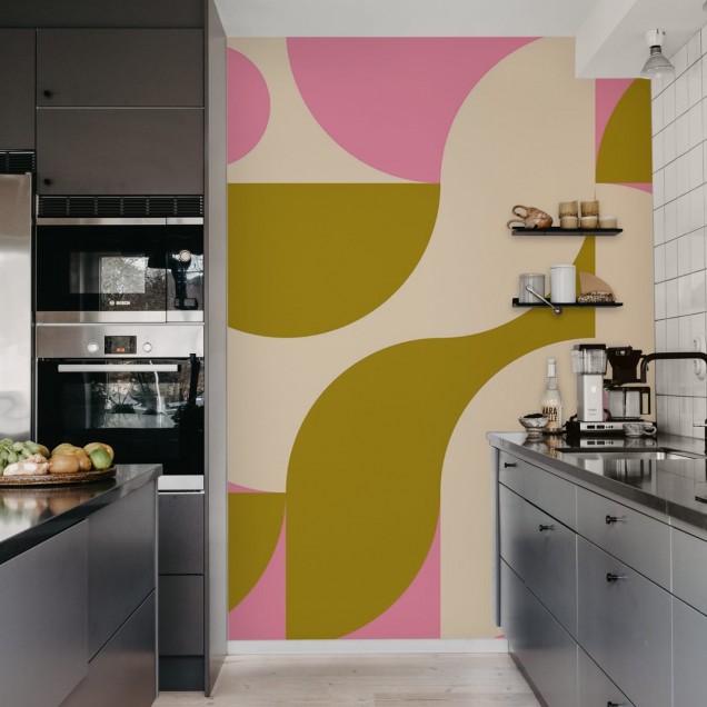 Tapet geometric modern, cu design vibrant, in tonuri pastelate de roz, galben si crem. Tapetul este aplicat pe un perete din camera de zi, decorata cu mobilier modern.