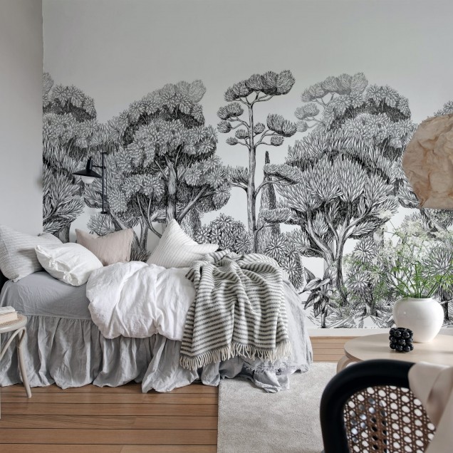 Tapet Forest Park Graphite cu un design minimalist ce prezintă copaci în tonuri de gri. Tapetul este aplicat pe un perete într-o sufragerie modernă cu o masă din lemn, scaune negre și o lampă cu abajur din hârtie.