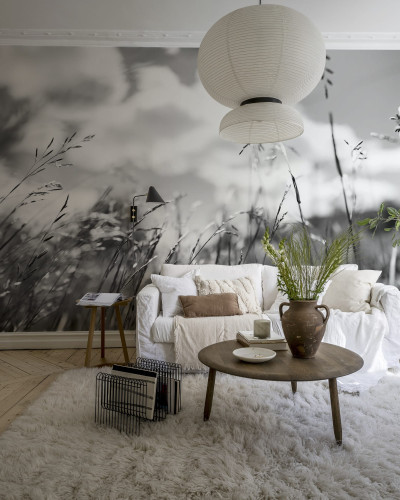 Wallpaper cu o imagine minimalistă, in tonuri de gri, a unor fire de iarbă, decorand o cameră cu un canapea, o măsuță de cafea, o lampă și o plantă.
