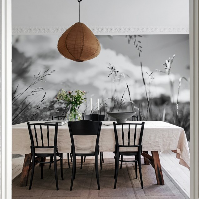 Wallpaper cu o imagine minimalistă, in tonuri de gri, a unor fire de iarbă, decorand o cameră cu un canapea, o măsuță de cafea, o lampă și o plantă.
