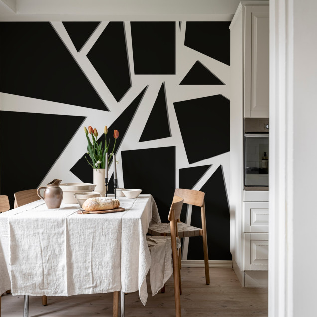 Tapet geometric abstract în culori negru și alb, aplicat pe un perete din living, lângă o canapea albă, cu un covor alb și un fotoliu maro.