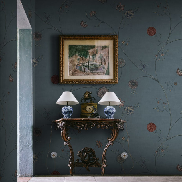 Wallpaper floral in nuante de albastru, cu flori delicate si ramuri subtiri, incadrand o masa cu scaune intr-o camera luminoasa.
