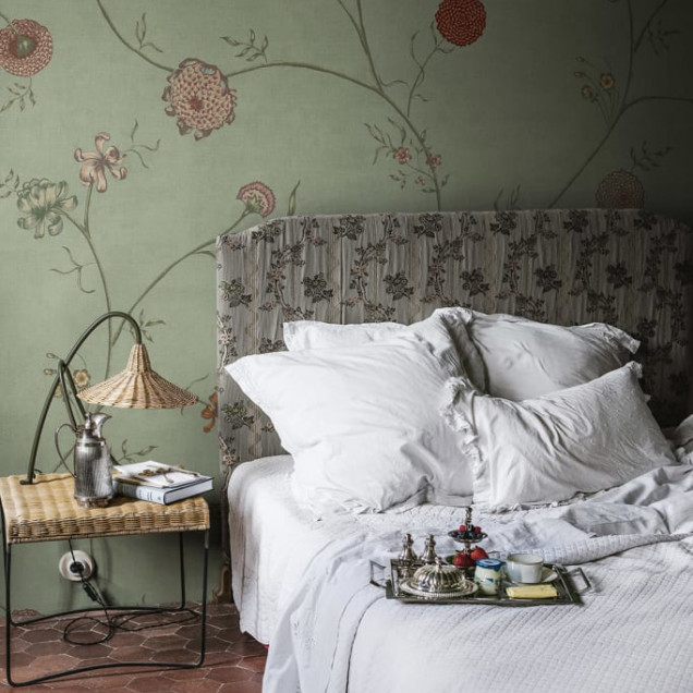 Tapet Grand Flower Thread cu flori delicate pe un fundal verde. Imaginea prezintă un tapet aplicat pe un perete din living, cu o masă de dining și scaune.