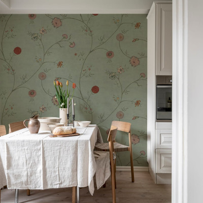 Tapet Grand Flower Thread cu flori delicate pe un fundal verde. Imaginea prezintă un tapet aplicat pe un perete din living, cu o masă de dining și scaune.