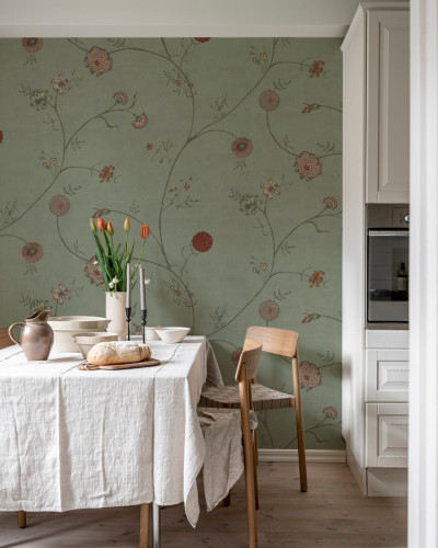Tapet Grand Flower Thread cu flori delicate pe un fundal verde. Imaginea prezintă un tapet aplicat pe un perete din living, cu o masă de dining și scaune.