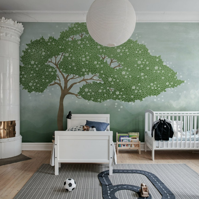 Tapet cu design unic, Windy Tree Green, cu un copac verde cu frunze bogate, flori albe delicate si un fundal bleu deschis.
