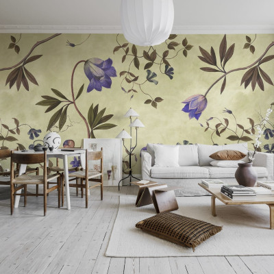 Tapet floral cu flori delicate, de un lila vibrant, pe un fundal verde deschis. Tapetul este aplicat pe un perete din living, lângă o canapea albă și o masă de cafea.