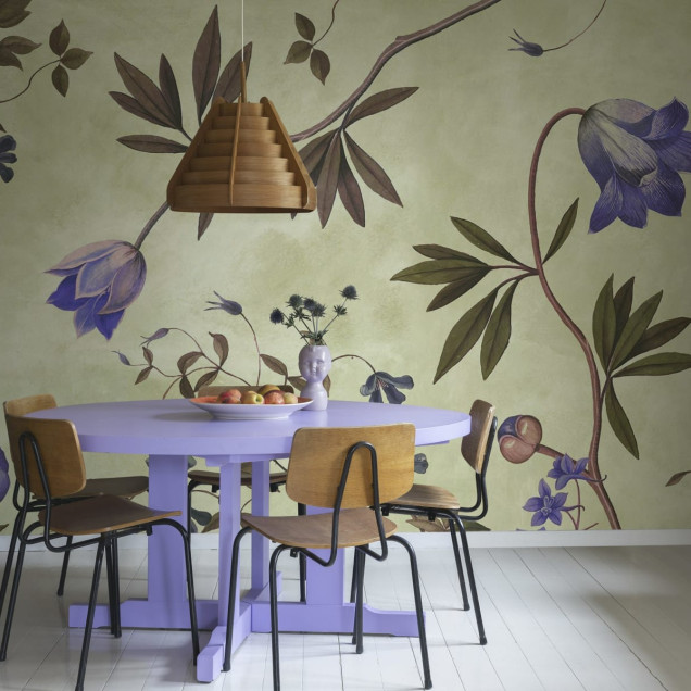 Tapet floral cu flori delicate, de un lila vibrant, pe un fundal verde deschis. Tapetul este aplicat pe un perete din living, lângă o canapea albă și o masă de cafea.