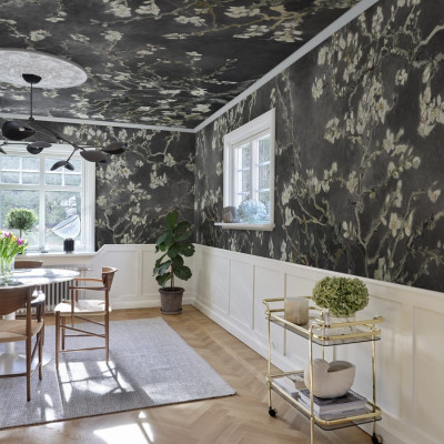 Tapet cu flori de migdal albe pe fundal negru, aplicat pe un perete intr-un living modern.